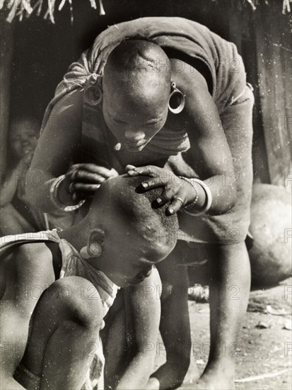 A Kikuyu mother de-louses her daughter. A Kikuyu mother bends over to de-louse her daughter's shaven head. South Nyeri, Kenya, 1936. Nyeri, Central (Kenya), Kenya, Eastern Africa, Africa.