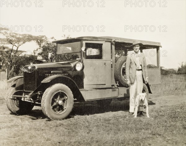A Ford box-body car. A European man and his dog pose beside a Ford box-body car. Kenya, circa 1928. Kenya, Eastern Africa, Africa.