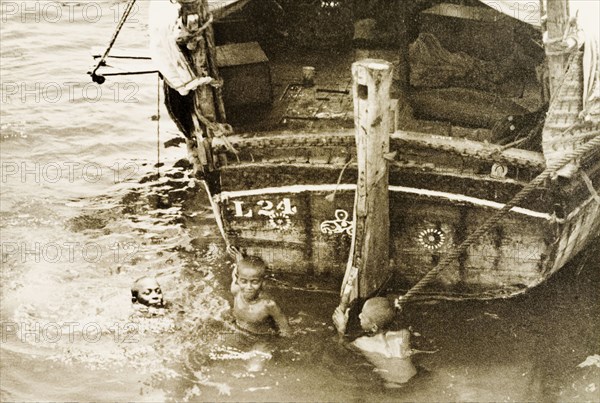 Children playing in Old Mombasa harbour. Three children play at the stern of a dhow in the shallow waters of Old Mombasa harbour. Mombasa, Kenya, 1933. Mombasa, Coast, Kenya, Eastern Africa, Africa.