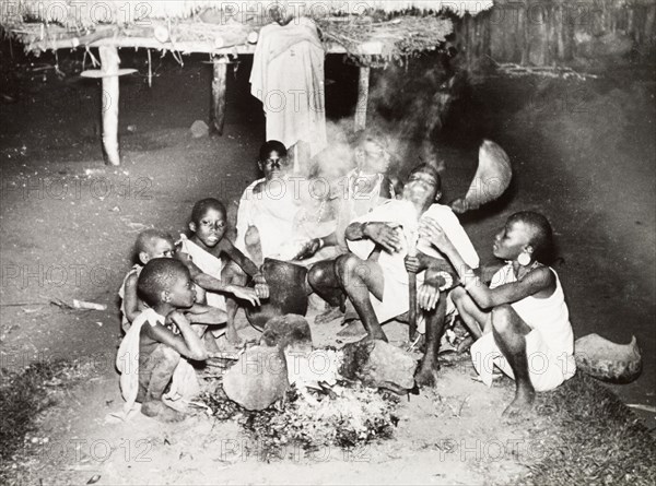 A Kikuyu family gather around a fire. A Kikuyu family gather around a smoky outdoor fire to eat their evening meal. Nyeri, Kenya, 1936. Nyeri, Central (Kenya), Kenya, Eastern Africa, Africa.