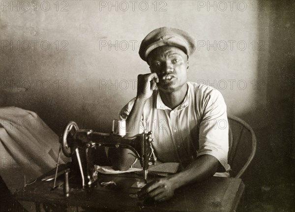 A Swahili tailor. A Swahili tailor sits behind a sewing machine at his work desk in Mombasa. Mombasa, Kenya, 1947. Mombasa, Coast, Kenya, Eastern Africa, Africa.