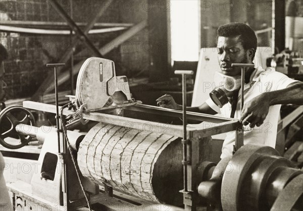 Craftsman operating a lathe, Ghana. A craftsman operates a wood-turning lathe to shape a section of timber into the shell of an atumpan drum. Ghana, circa 1965. Ghana, Western Africa, Africa.