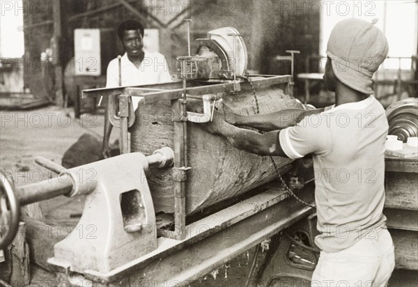 Craftsman operating a lathe, Ghana. A craftsman operates a wood-turning lathe to shape a section of timber into the shell of an atumpan drum. Ghana, circa 1965. Ghana, Western Africa, Africa.