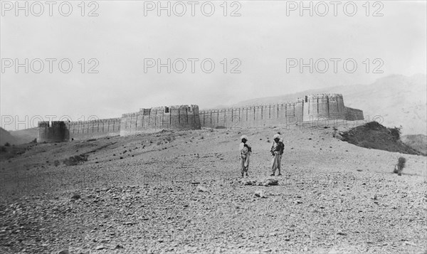 Fort wall in Kohistan . Two turbaned figures stand outside a hill fort in Kohistan, which features a strong defensive outer wall and round, crenellated watchtowers. Kohistan, North West Frontier Province, India (Pakistan), circa 1915. Kohistan, North West Frontier Province, Pakistan, Southern Asia, Asia.