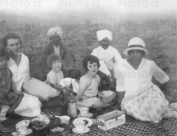 A family picnic in India. A British family enjoys a picnic outdoors, accompanied by three Indian servants including Nannie, their ayah (nursemaid). India, circa 1925. India, Southern Asia, Asia.