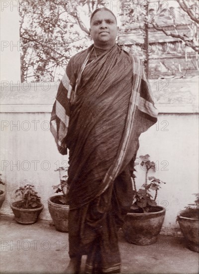 Portrait of an Indian man. An Indian man in traditional, possibly religious robes, poses outdoors beside a row of potted plants. Karachi, Sind, India (Sindh, Pakistan), circa 1910. Karachi, Sindh, Pakistan, Southern Asia, Asia.