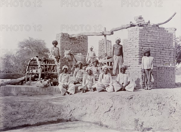 A bullock-driven water wheel, India. A group of Indian labourers pose for an outdoor portrait beside a bullock-driven water wheel. India, circa 1925. India, Southern Asia, Asia.