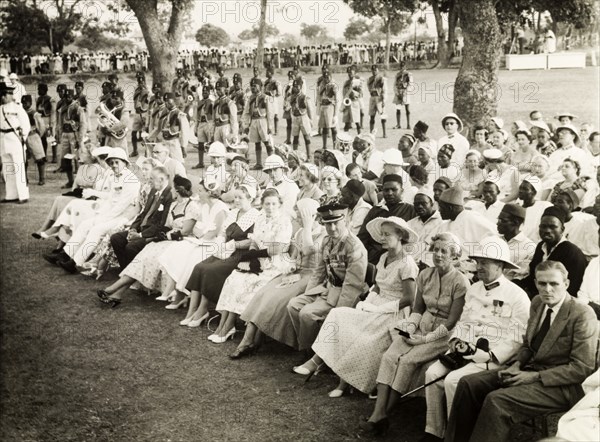 Awaiting Queen Elizabeth II's arrival. A seated assembly of African and European dignitaries await the arrival of Queen Elizabeth II at Lugard Hall, whilst the Nigeria Regiment's military band prepare to play. Kaduna, Nigeria, 3 February 1956. Kaduna, Kaduna, Nigeria, Western Africa, Africa.