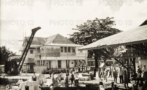 Unloading goods at Apia wharf. Crates of goods are unloaded from barges at a wharf in the port city of Apia. Apia, Western Samoa (Samoa), circa 1956. Apia, Apia Urban Area, Samoa, Pacific Ocean, Oceania.