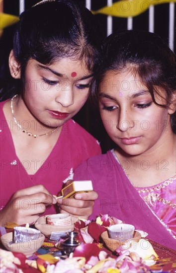 Lighting candles for Diwali. Two girls in traditional Indian dress light candles to celebrate Diwali, the Hindu festival of light, during a mela (fair) at the Commonwealth Institute. London, England, circa 1985. London, London, City of, England (United Kingdom), Western Europe, Europe .