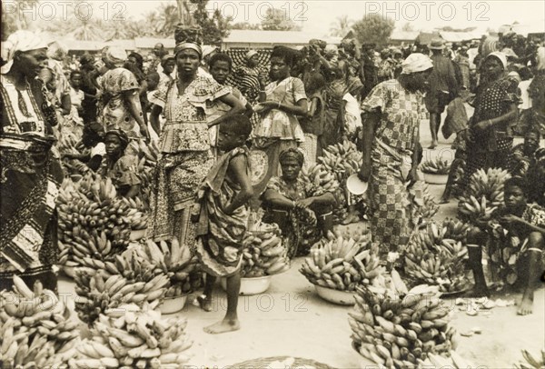 Banana stalls at a busy marketplace. Female traders sell hands of bananas from bowls at a bustling marketplace. Volta Region, Gold Coast (Ghana), circa 1950., Volta, Ghana, Western Africa, Africa.