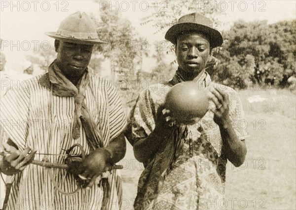 The chief's musicians'. Two men, described in an original caption as "the chief's musicians", play traditional West African string and percussion instruments. Gold Coast (Ghana), circa 1950. Ghana, Western Africa, Africa.