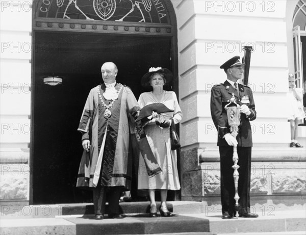 The Mayor and Mayoress of Nairobi. The Mayor of Nairobi stands on the steps of City Hall with his wife, dressed in full mayoral regalia, as he awaits the arrival of Princess Elizabeth and the Duke of Edinburgh. An official stands to their left, holding a ceremonial staff. Nairobi, Kenya, February 1952. Nairobi, Nairobi Area, Kenya, Eastern Africa, Africa.