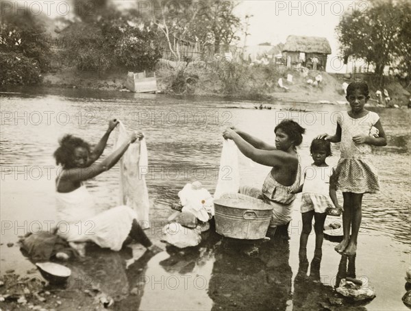 Washing clothes in a stream. Two female plantation workers, accompanied by two young girls, sit in a shallow stream washing their clothes. Trinidad and Tobago, circa 1931., Trinidad and Tobago, Trinidad and Tobago, Caribbean, North America .