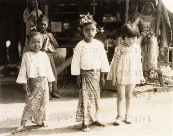 Children in Rangoon. A young British girl poses with two Burmese children wearing traditional 'longyis' on a city street in Rangoon. Rangoon, Burma (Yangon, Myanmar), 1931. Yangon, Yangon, Burma (Myanmar), South East Asia, Asia.