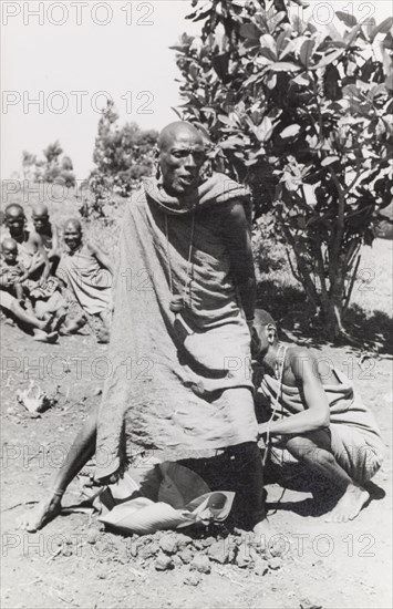 Kikuyu purification ceremony. A Kikuyu witch doctor performs a traditional purification ceremony to absolve a man of his sins. In this ritual, the perpetrator is fed a concoction of herbs and minerals, mixed with the undigested stomach contents from a sacrificed goat. The mixture is then spat or vomited out to cleanse the offender of their sins. South Nyeri, Kenya, 1936. Nyeri, Central (Kenya), Kenya, Eastern Africa, Africa.