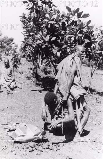 Kikuyu purification ceremony. A Kikuyu witch doctor performs a traditional purification ceremony to absolve a man of his sins. In this ritual, the perpetrator is fed a concoction of herbs and minerals, mixed with the undigested stomach contents from a sacrificed goat. The mixture is then spat or vomited out to cleanse the offender of their sins. South Nyeri, Kenya, 1936. Nyeri, Central (Kenya), Kenya, Eastern Africa, Africa.