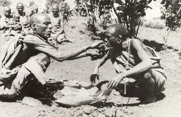 Kikuyu purification ceremony. A Kikuyu witch doctor performs a traditional purification ceremony to absolve a man of his sins. In this ritual, the perpetrator is fed a concoction of herbs and minerals, mixed with the undigested stomach contents from a sacrificed goat. The mixture is then spat or vomited out to cleanse the offender of their sins. South Nyeri, Kenya, 1936. Nyeri, Central (Kenya), Kenya, Eastern Africa, Africa.