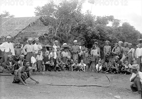 Snake charmer's performance. Two street performers entertain a crowd of onlookers with a snake charming show. Burma (Myanmar), circa 1890. Burma (Myanmar), South East Asia, Asia.