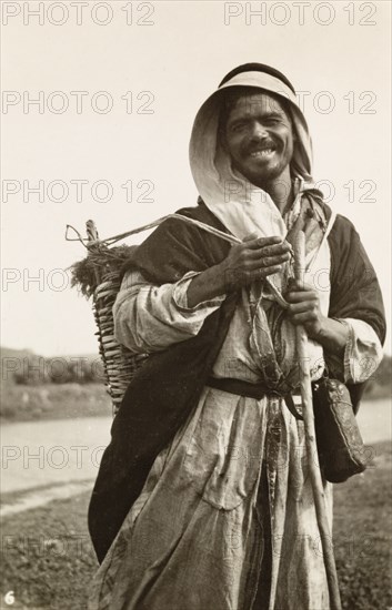 Portrait of a Palestinian bedouin man. Portrait of a smiling bedouin man, who carries a large basket strapped on his back as he travels along a rural road. British Mandate of Palestine (Middle East), circa 1942., Middle East, Asia.