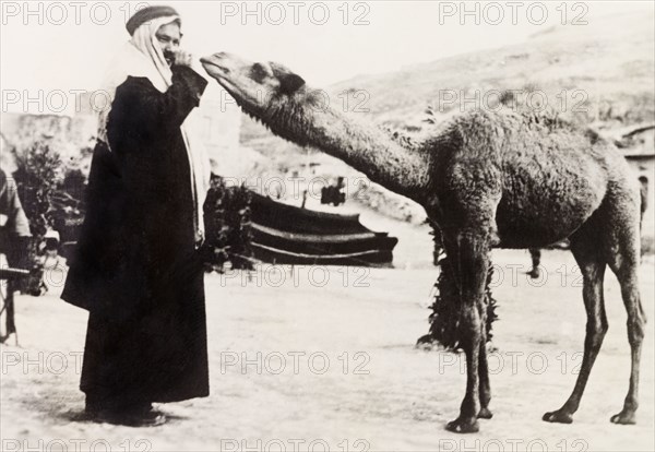 A curious camel. An Arab man in traditional Arab dress poses with an inquisitive camel. British Mandate of Palestine (Middle East), circa 1938., Middle East, Asia.