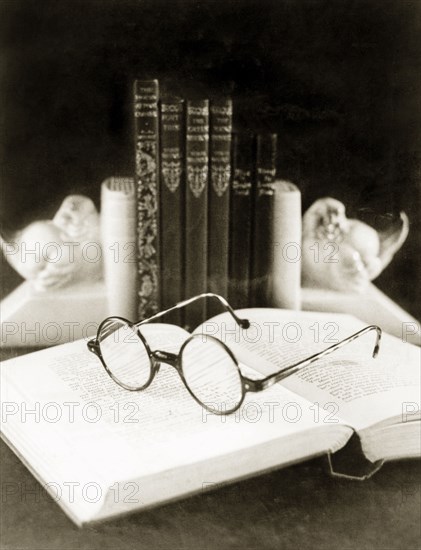 Front cover for a catalogue by 'James Murray & Co.'. Still life study of a pair of spectacles positioned on an open book. This photograph was taken for the front cover of a catalogue by 'James Murray & Co.', a British-owned family business that specialised in making chronometers and also operated as a jewellers and opticians. Calcutta (Kolkata), India, circa 1934. Kolkata, West Bengal, India, Southern Asia, Asia.