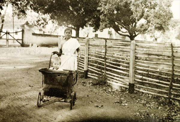 Indian ayah taking her charge for a walk. An Indian ayah (nursemaid) pushes British toddler Nell Sargant in a pram past the grounds of Chikmagalur Church, where her father serves as a Methodist Reverend. Chikmagalur, Mysore State (Chikkamagaluru, Karnataka), India, 1938., Karnataka, India, Southern Asia, Asia.