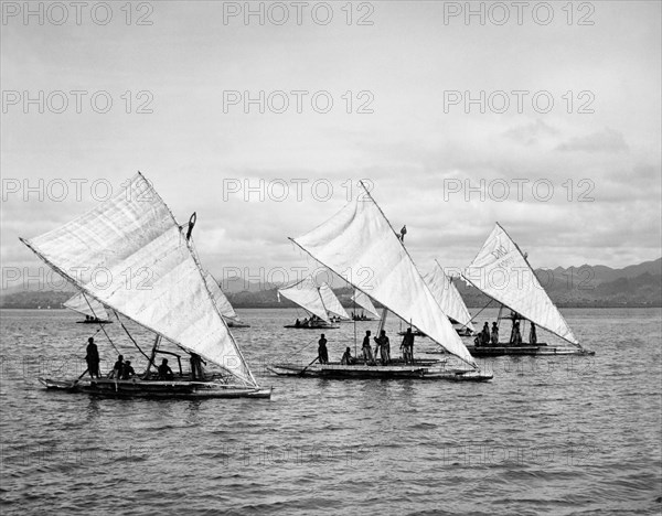 Druas' off the coastline of Fiji. A flotilla of at least ten 'druas' (Fijian catamarans) sails off the coastline of Fiji. Fiji, 1965. Fiji, Pacific Ocean, Oceania.