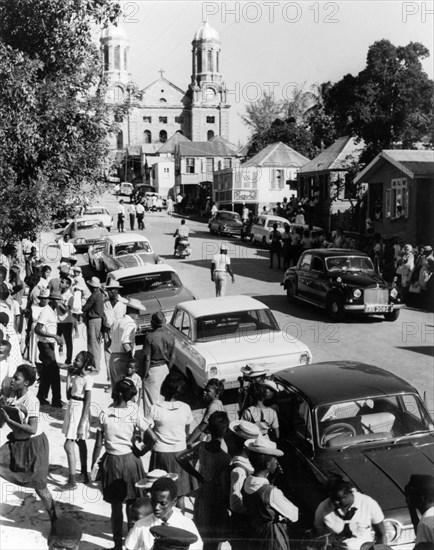 Waiting for the carnival to start. Expectant crowds gather on the main street in St John's, waiting for a carnival procession to begin. The twin white baroque towers of St John's Cathedral are visible in the distance. St Johns, Antigua, 1965. St John's, St John (Antigua and Barbuda), Antigua and Barbuda, Caribbean, North America .