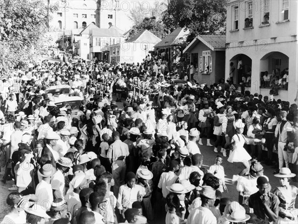 Carnival procession in St John's. Crowds pack the main street in St John's during a carnival procession through the centre of town. St John's Cathedral is just visible in the distance. St Johns, Antigua, 1965. St John's, St John (Antigua and Barbuda), Antigua and Barbuda, Caribbean, North America .