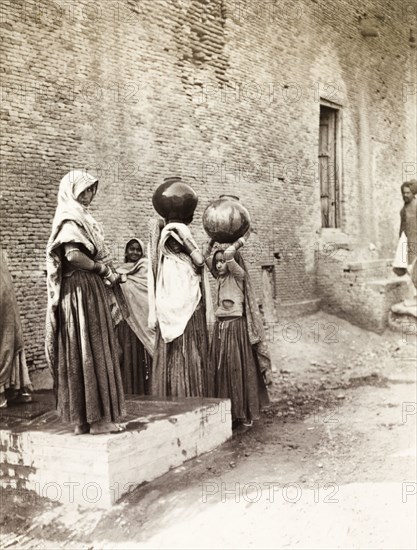 Women collecting water, Agra. A group of young Indian women collect water from a communal pump in Agra, which they carry in large ceramic pots balanced on their heads. Agra, United Provinces (Uttar Pradesh), India, December 1902. Agra, Uttar Pradesh, India, Southern Asia, Asia.