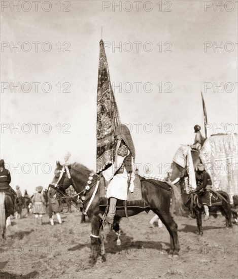 Flag bearer at Coronation Durbar, 1903. A mounted standard-bearer holds up an Indian princely state flag at Edward VII's Coronation Durbar. The bearer wears an armoured helmet featuring metal plates which taper down his back to protect his neck. Delhi, India, circa 1 January 1903. Delhi, Delhi, India, Southern Asia, Asia.