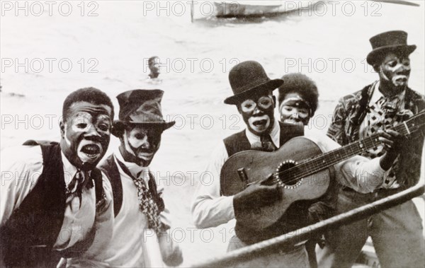 Blackface' calypso singers, Trinidad. A band of Trinidadian calypso singers put on a 'blackface' performance to the accompaniment of a guitar. They wear white face paint and theatrical clothing including patterned waistcoats and ties with top hats. Trinidad, circa 1930. Trinidad and Tobago, Caribbean, North America .