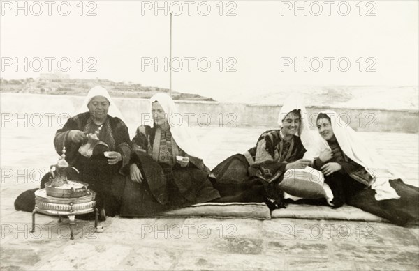 Women in traditional Palestinian attire. Four women sit on mats on a rooftop as they drink coffee together, dressed in traditional Palestinian 'thobs'. Related photographs show that the woman second from right had recently been married to Edward Keith-Roach, District Governor of Jerusalem, in a traditional Christian ceremony. Jerusalem, British Mandate of Palestine (Israel), circa 1939. Jerusalem, Jerusalem, Israel, Middle East, Asia.