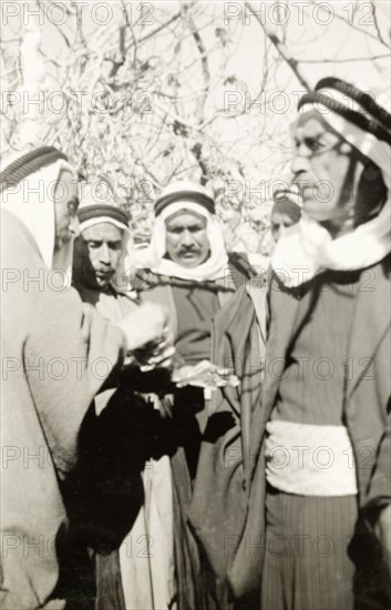 Arab villagers exchange money. Arab villagers wearing 'keffiyehs' (headdresses) exchange money during a meeting with William Ryder McGeagh, District Commissioner in Jerusalem. British Mandate of Palestine (Israel), circa 1940. Israel, Middle East, Asia.