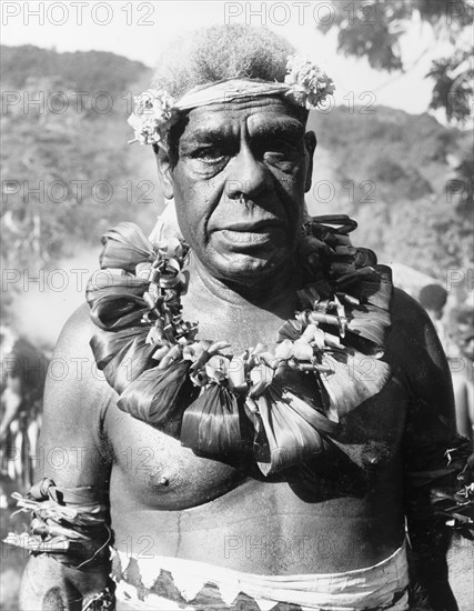 Portrait of a Fijian chief. Head and shoulders portrait of a Fijian chief wearing ceremonial costume. Naked from the waist up, he wears a lei of twisted palm leaves around his neck and a simple floral headband. Fiji, 1965. Fiji, Pacific Ocean, Oceania.