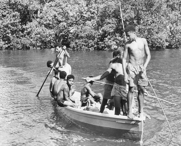 Boys in a canoe, Fiji. A group of boys in shorts relax in the sun as they pilot a canoe along a river. Levuka, Ovalau, Fiji, 1965. Levuka, Ovalau, Fiji, Pacific Ocean, Oceania.