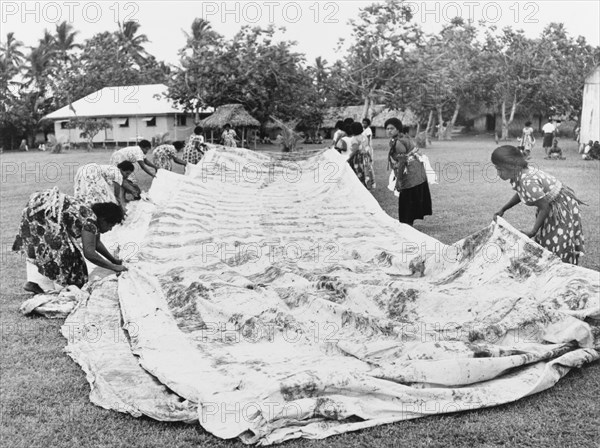 Laying out a 'masi' cloth. A group of Fijian women lay out a finished 'masi' or 'tapa' cloth, made from the bark of the paper mulberry tree (Broussonetia papyrifera). Once completed, tapa is painted or dyed with patterns and motifs, and used for traditional clothing or decoration. Fiji, 1965. Fiji, Pacific Ocean, Oceania.