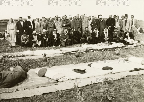 Recruitment meeting at Al Faluja. British colonial and military officers pose for a group portrait with Arab villagers at a military recruitment meeting. In front of them on the ground are two rows of padded mats and cushions, together with three water jugs. Al Faluja, British Mandate of Palestine (South Israel), 1944., South (Israel), Israel, Middle East, Asia.