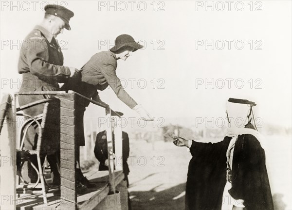 At a camel race in Be'er Sheva. The wife of William Ryder McGeagh, District Commissioner in Jerusalem, accepts a token from an Arab man during a camel race at Be'er Sheva. The man in uniform to her right is identified as 'Cullingham'. Be'er Sheva, British Mandate of Palestine (South Israel), 27 February 1944. Be'er Sheva, South (Israel), Israel, Middle East, Asia.