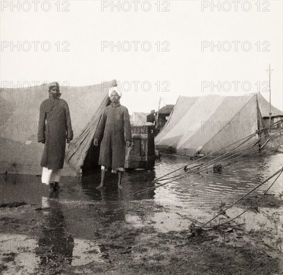 Flood at an Indian Police camp. Two Indian men stand in front of flooded tents at the James Ferguson camp, Indian Police, ankle-deep in muddy water after a heavy storm. United Provinces (Uttar Pradesh), India, 1936., Uttar Pradesh, India, Southern Asia, Asia.