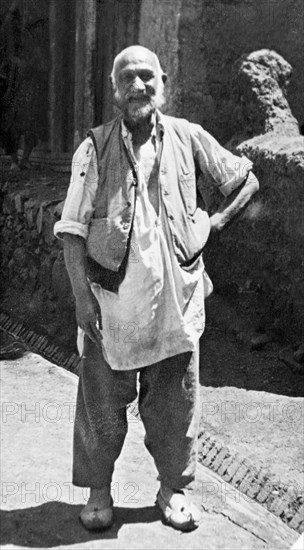 A Kashmiri 'dhobi'. Full-length portrait of a Kashmiri dhobi' (laundryman) dressed in a loose tunic, a waistcoat and curly-toed shoes. Srinagar, Jammu and Kashmir, India, 1934. Srinagar, Jammu and Kashmir, India, Southern Asia, Asia.