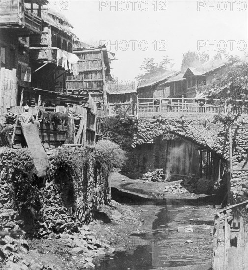 The Mar Canal in Srinigar. A trickle of water runs past ramshackle buildings and beneath a small stone bridge at the Mar Canal, one of Srinagar's most ancient canals, which was later filled in and converted to become a double-lane road. Srinagar, Jammu and Kashmir, India, 1934. Srinagar, Jammu and Kashmir, India, Southern Asia, Asia.