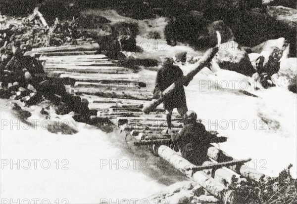 Constructing a timber bridge near Sekwas Pass. Two Kashmiri mountain guides construct a makeshift timber bridge across a fast-flowing mountain river near Sekwas Pass. Jammu and Kashmir, India, 1934., Jammu and Kashmir, India, Southern Asia, Asia.