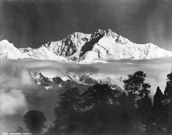 Kanchenjunga, circa 1919. The snow-capped peaks of Kanchenjunga mountain rise up above a layer of cloud. India-Nepal border, circa 1919. India, Southern Asia, Asia.