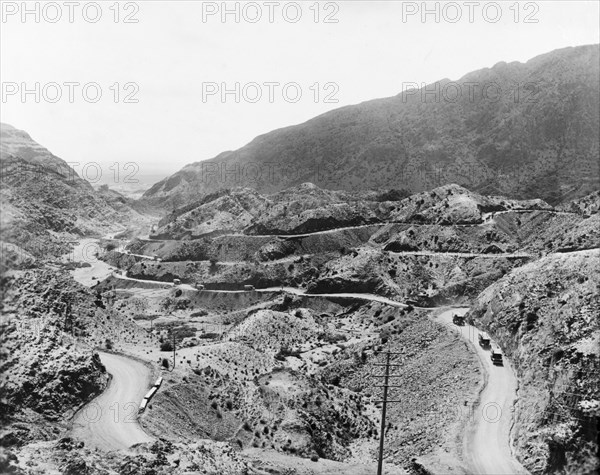 Roads at the mouth of the Khyber Pass. Indian Army trucks and a convoy of camels travel along winding mountain roads at the mouth of the Khyber Pass. An original caption points out the Peshawar Plains in the distance. North West Frontier Province, India (Federally Administered Tribal Areas, Pakistan), 1919., Federally Administered Tribal Areas, Pakistan, Southern Asia, Asia.