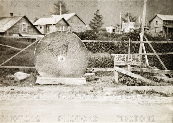 The Russian 'Community Grindstone' at Sitka . A large grindstone stands upright beside a road in Sitka, accompanied by a sign that reads: 'Community Grindstone used by the Russian Colony in 1830'. Sitka, Alaska, United States of America, circa 1931. Sitka, Alaska, United States of America, North America, North America .