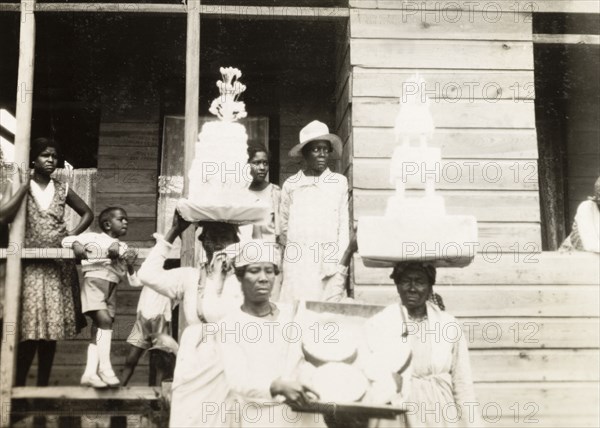 Wedding cakes in Trinidad. Two Trinidadian women balance tiered wedding cakes on their heads as they transport food to a nearby wedding reception. Siparia, Trinidad, circa 1931. Siparia, Trinidad and Tobago, Trinidad and Tobago, Caribbean, North America .