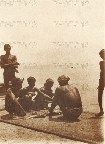 Boatmen on the breakwater. Boatmen cut up fish on the breakwater. Mormugao, Goa, India, circa 1906. Mormugao, Goa, India, Southern Asia, Asia.