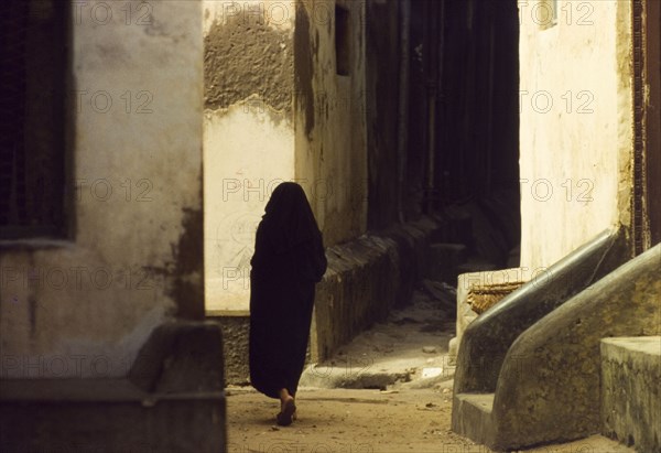 An alleyway in Mombasa. A robed figure walks through a winding alleyway in Mombasa. Mombasa, Kenya, April 1964. Mombasa, Coast, Kenya, Eastern Africa, Africa.